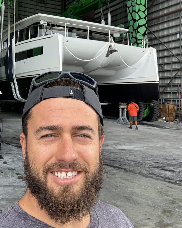 Damian Adcock in a boatyard, with a catamaran on a travel lift behind him.