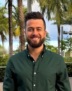 Head-and-shoulders photo of Damian Adcock, smiling, with palm trees behind him.